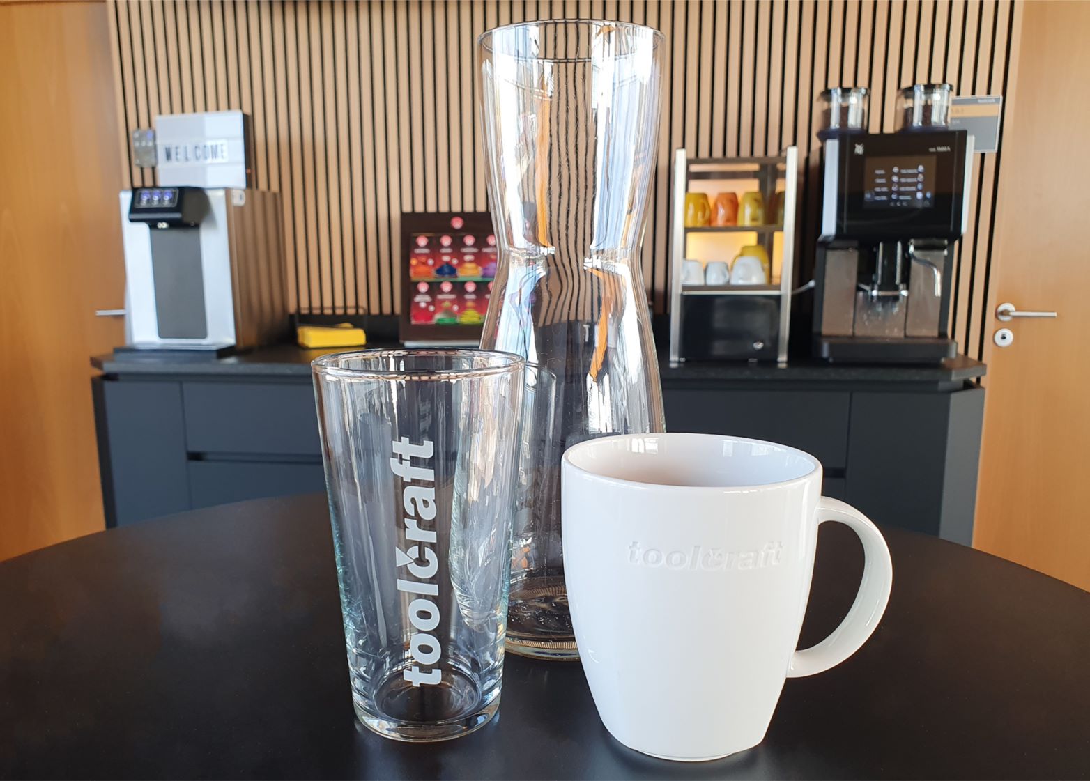 Glaskaraffe, Trinkglas und Kaffeebecher vor einer Kaffeemaschine und einem Wasserspender